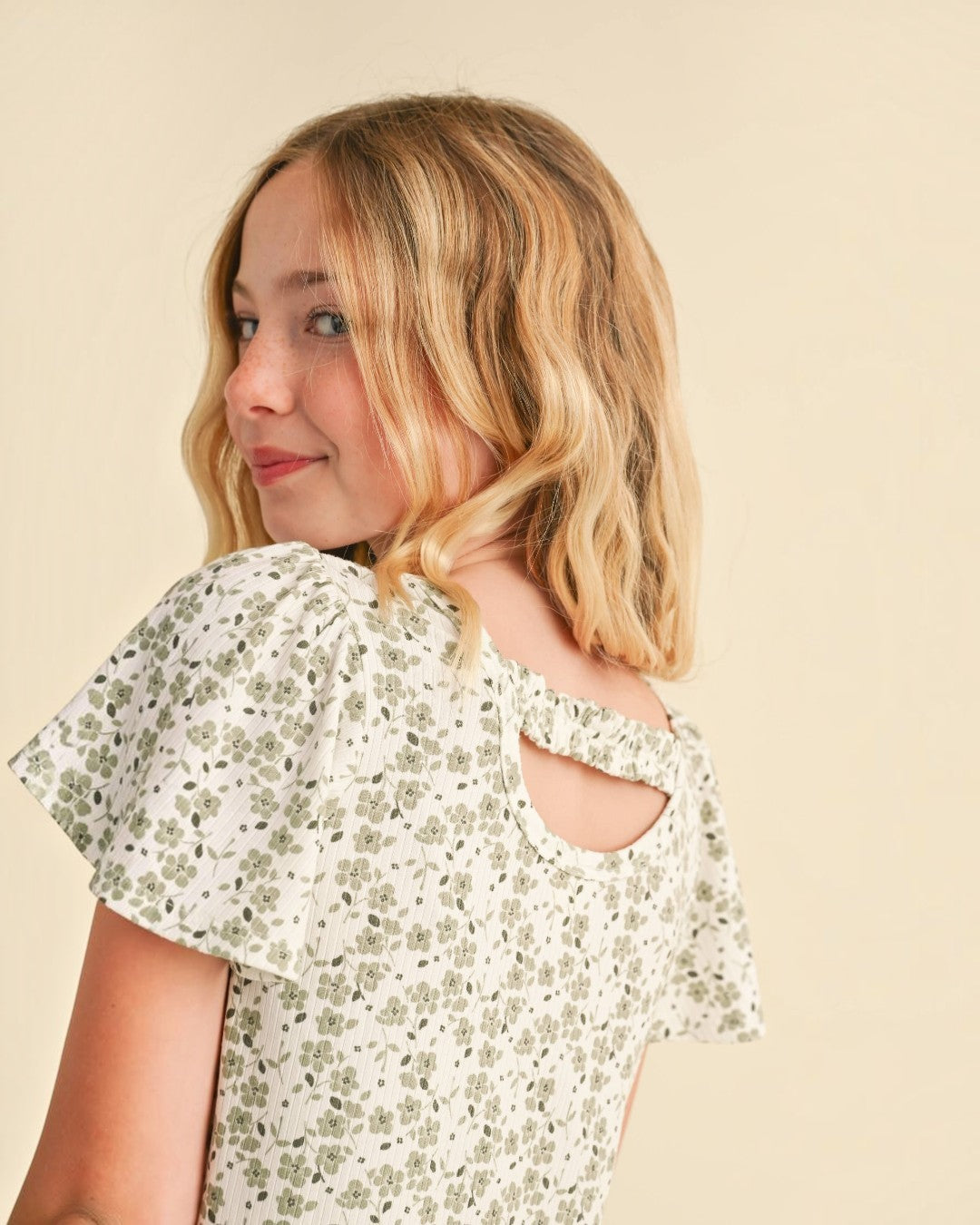 Young girl wearing a floral blouse with cut-out shoulders against a beige background