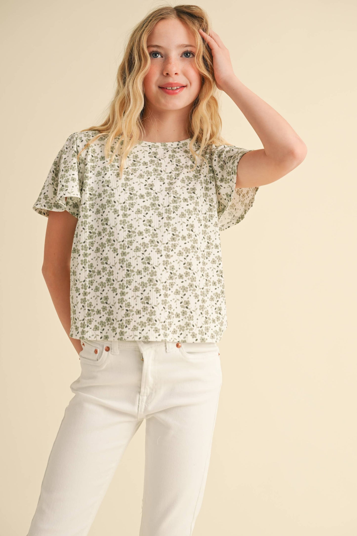Young girl wearing a floral blouse and white pants against a beige background