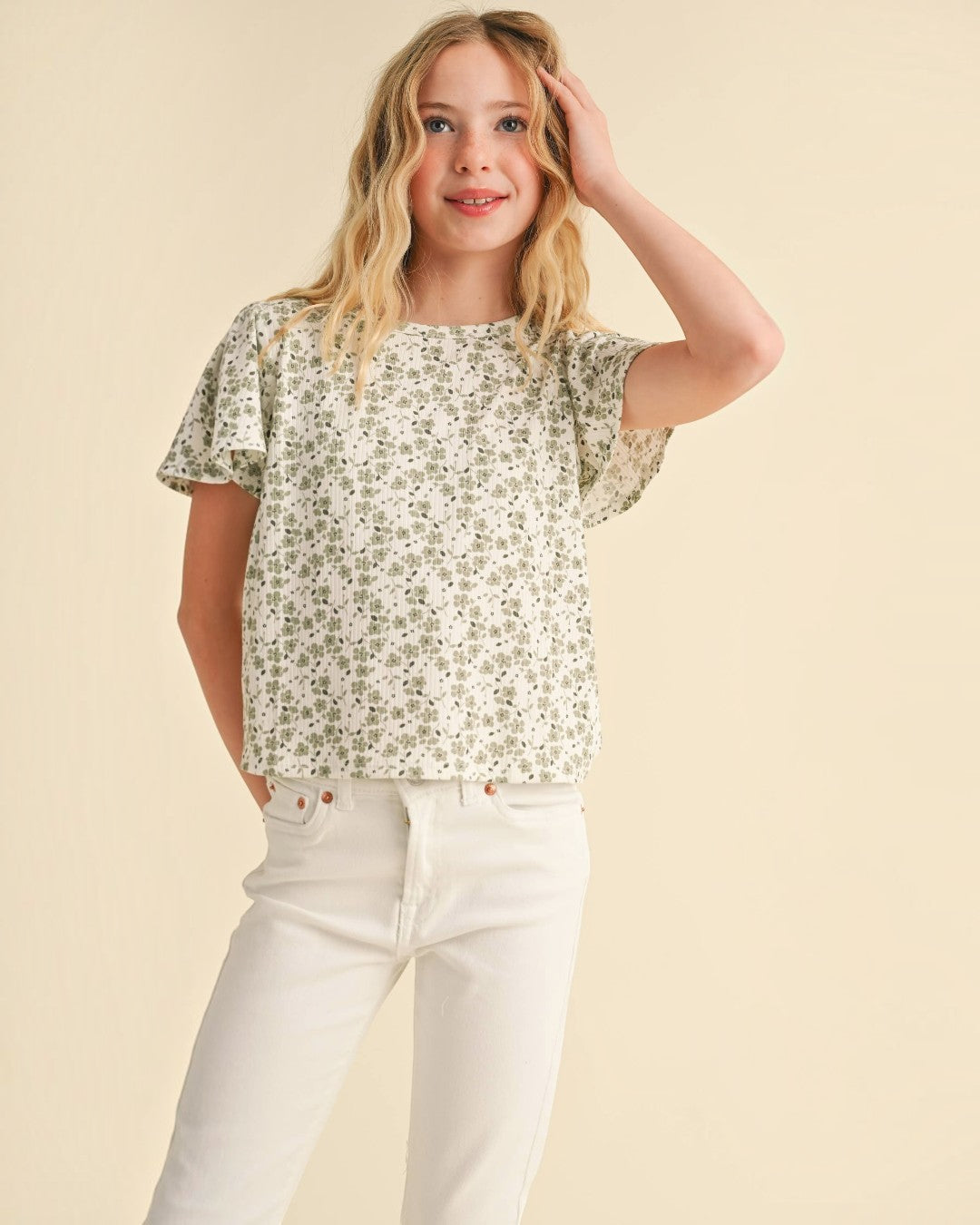 Young girl wearing a floral blouse and white pants against a beige background