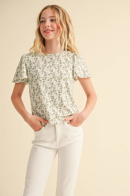 Young girl wearing a floral blouse and white pants on a beige background