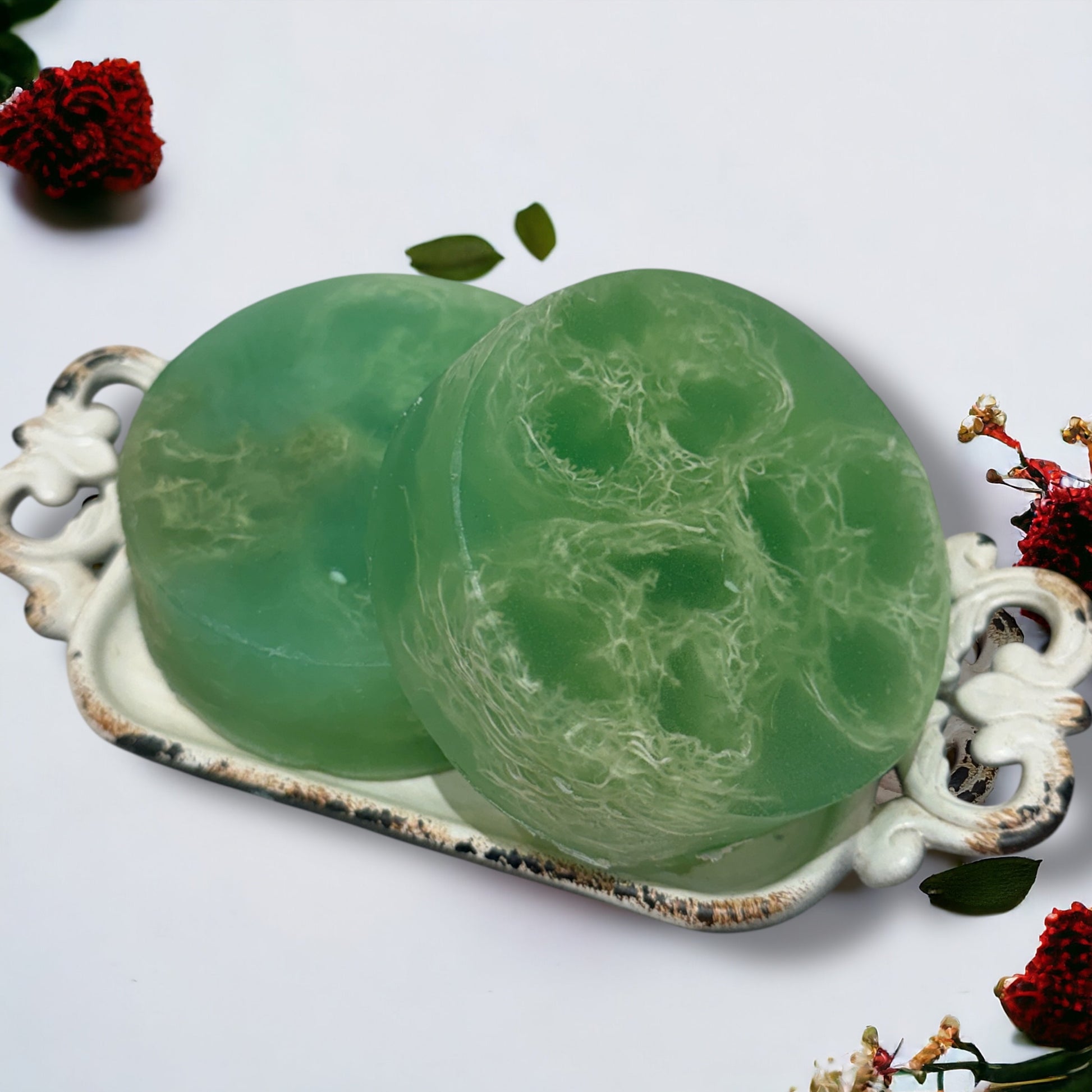 Two green marbled soap bars on a decorative white tray with floral elements.
