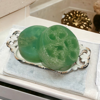 Two green marbled soap bars on a decorative silver tray with a white cloth background.