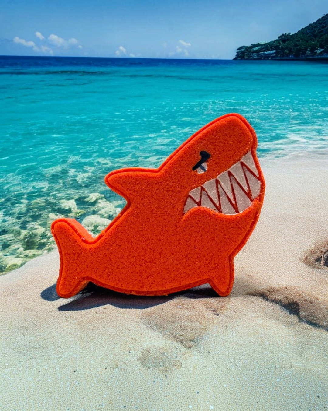 Calla Lily Cosmetics + CL kids red orange shark-shaped bath bomb with blood orange scent on a sandy beach