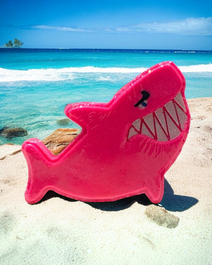 Calla Lily Cosmetics + CL kids pink shark-shaped strawberry-scented bath bomb on a sandy beach by the ocean.