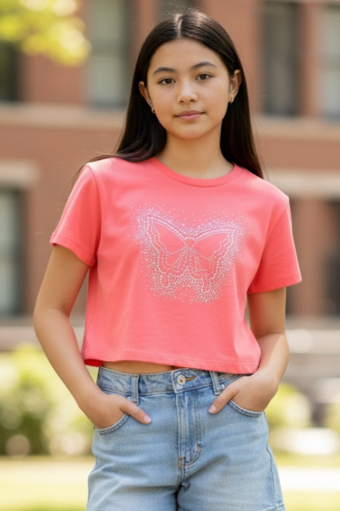 Young woman wearing a pink t-shirt and denim shorts standing outdoors with a blurred building in the background.