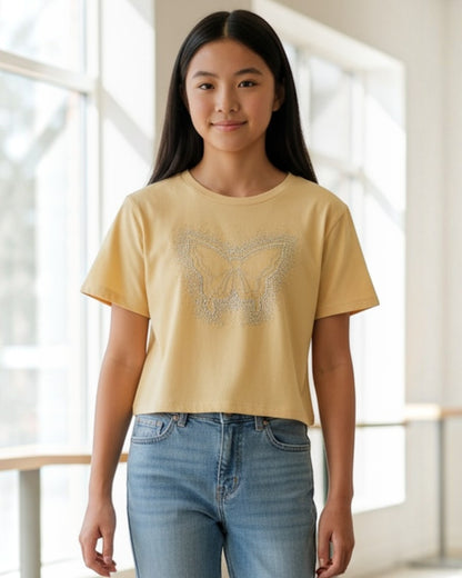 Person wearing a yellow t-shirt with a butterfly design and blue jeans in a bright indoor setting.