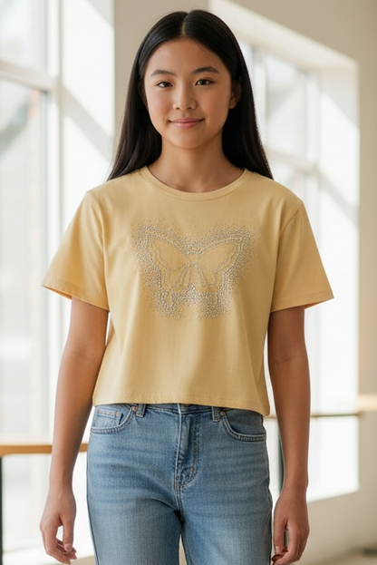 Person wearing a yellow t-shirt with a butterfly design and blue jeans in a bright indoor setting.