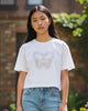 Woman wearing a white t-shirt with a graphic design and blue jeans standing in a garden.