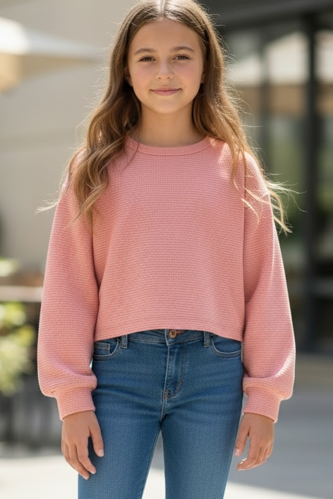 Young girl wearing a pink sweater and blue jeans standing outdoors.