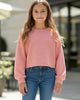 Young girl wearing a pink sweater and blue jeans standing outdoors.