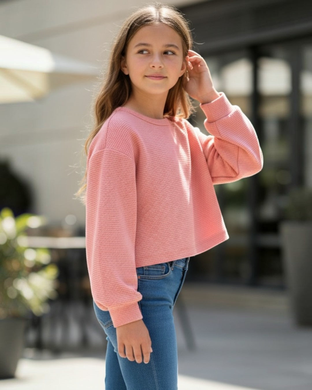Young girl wearing a pink sweater and blue jeans standing outdoors.