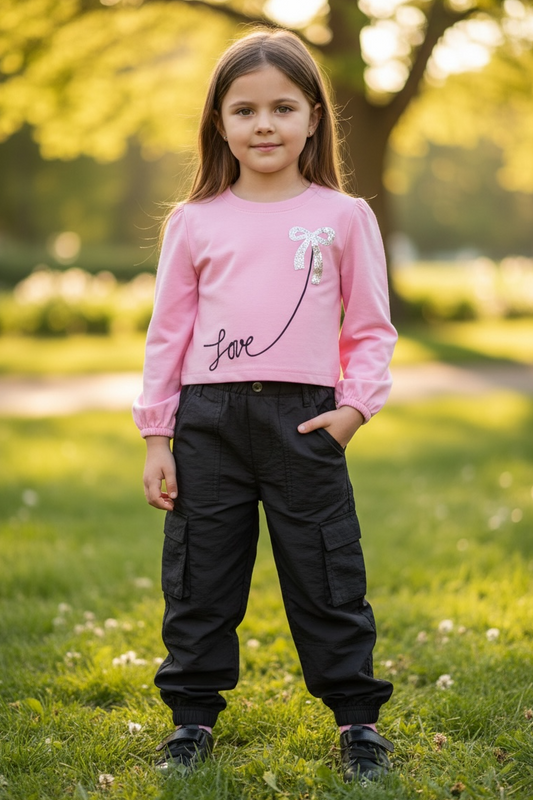 Young girl in a pink shirt and black pants standing in a park.