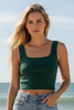 Woman in green top and denim shorts standing on a beach with ocean in the background