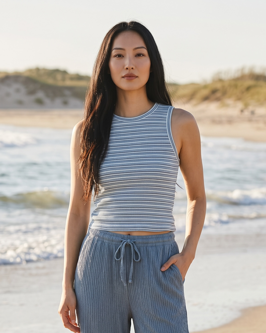 Woman in a striped sleeveless top and wide-leg pants standing on a beach.