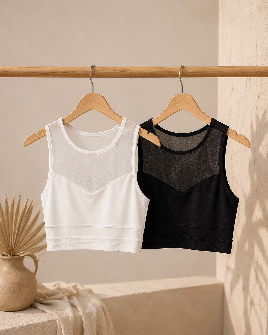 Two crop tops, one white and one black, hanging on a wooden rack against a neutral background.