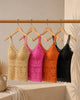 Five lace camisoles in gold, pink, orange, and black hanging on a rack against a neutral background.