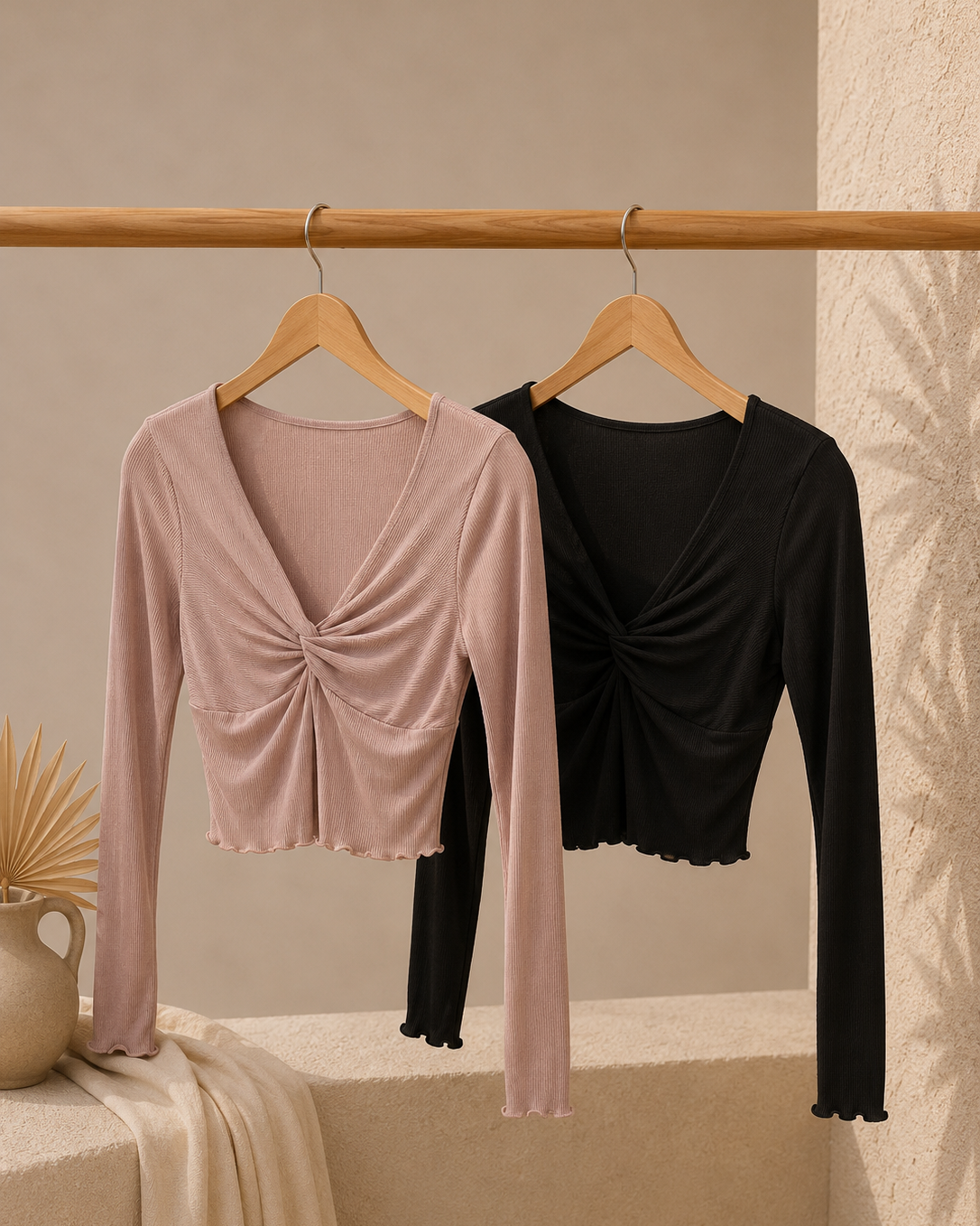 Two long-sleeve tops, one pink and one black, hanging on wooden hangers against a beige wall.