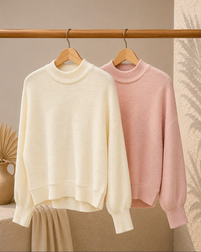 Two sweaters, one cream and one pink, hanging on a wooden rack against a neutral background.