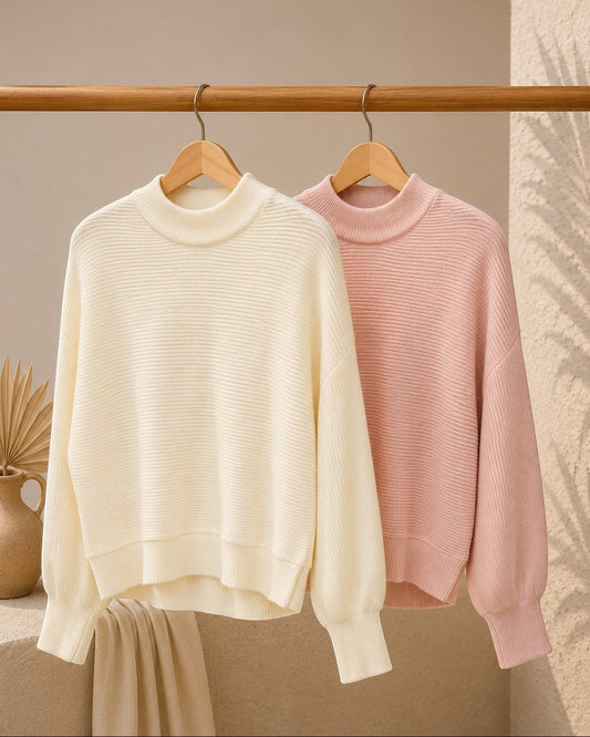 Two sweaters, one cream and one pink, hanging on a wooden rack against a neutral background.
