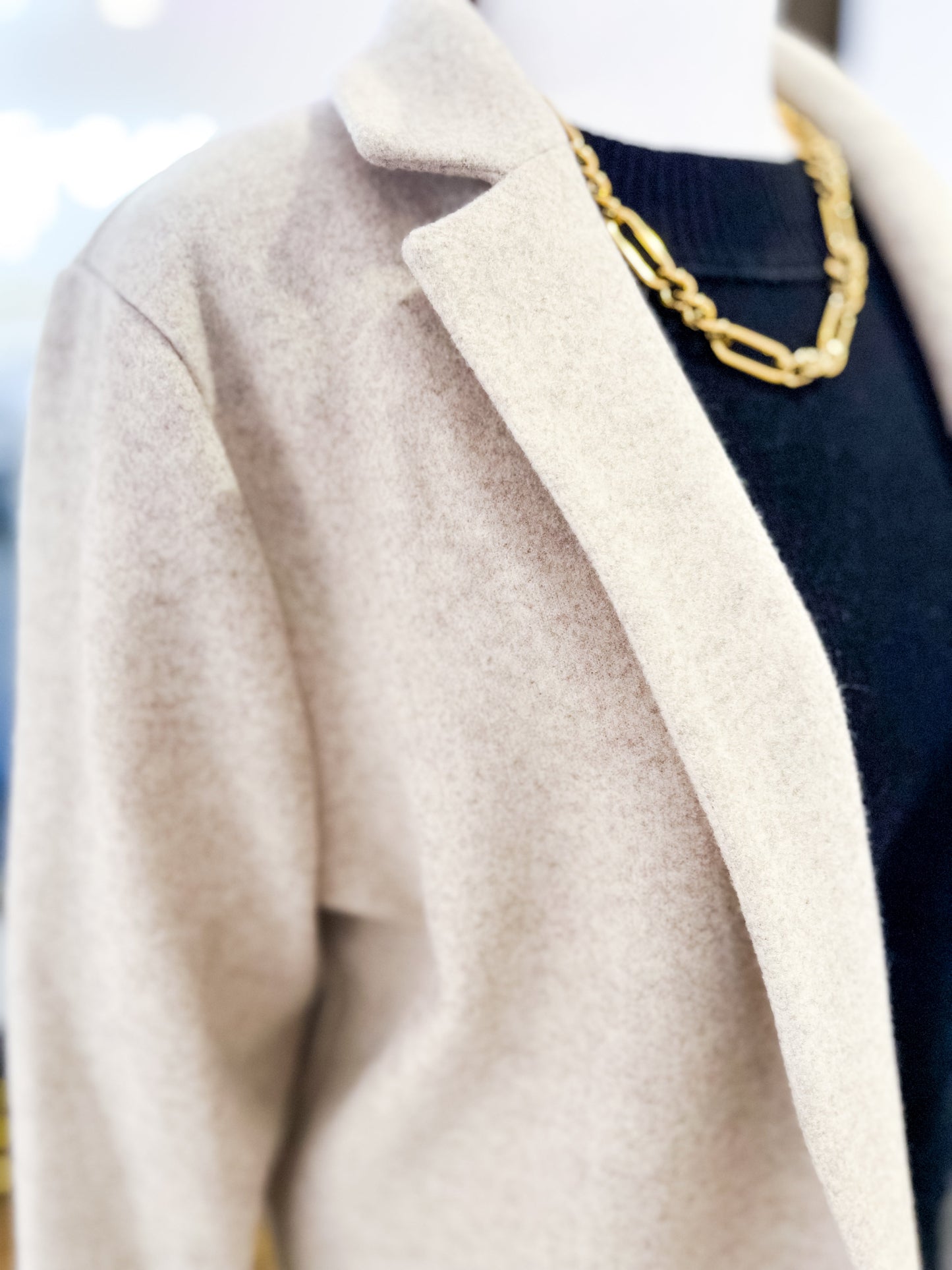 Close-up of a beige coat with a gold chain necklace and navy sweater.