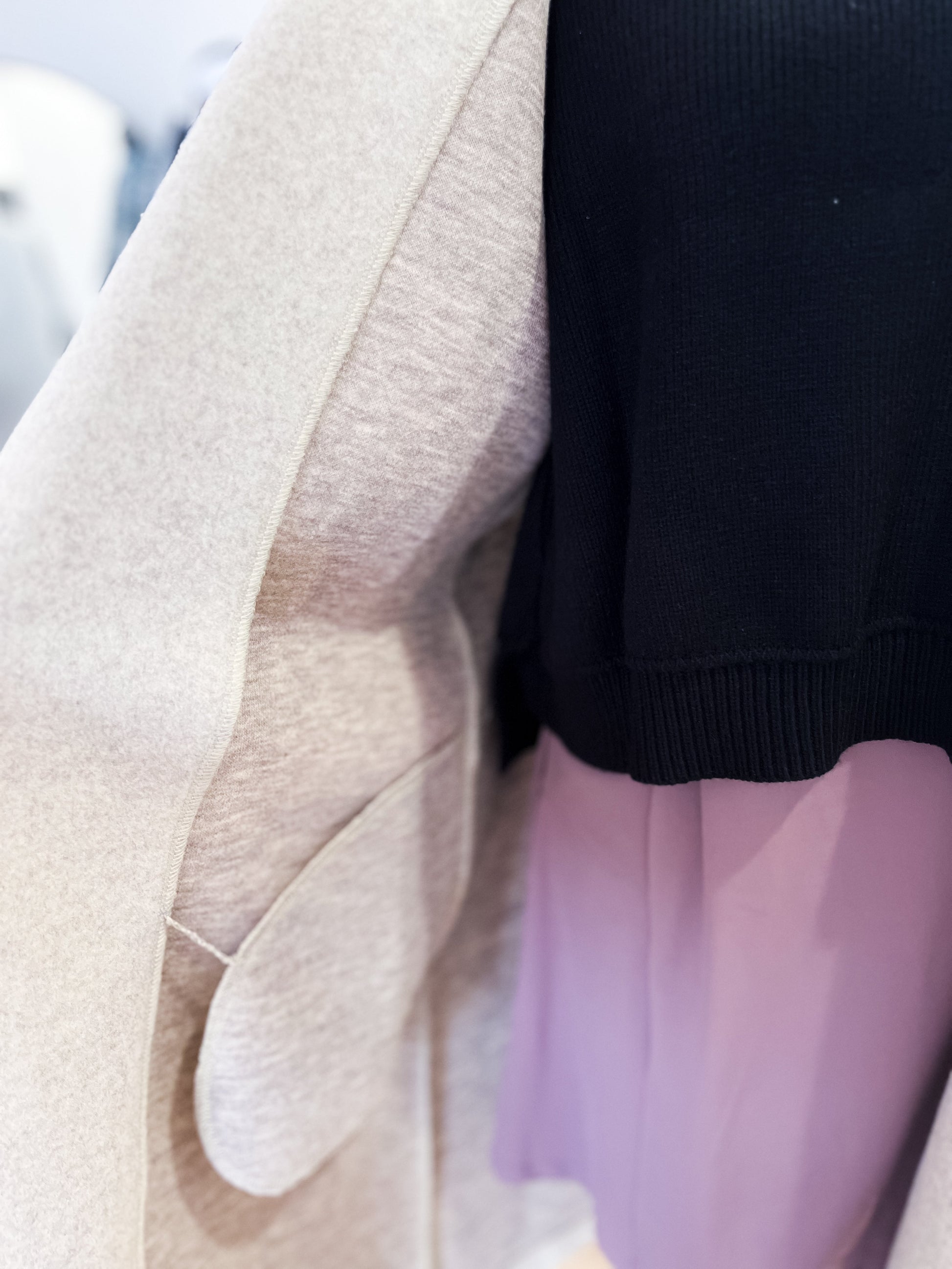 Close-up of a person wearing a beige sweater, black top, and pink pants.