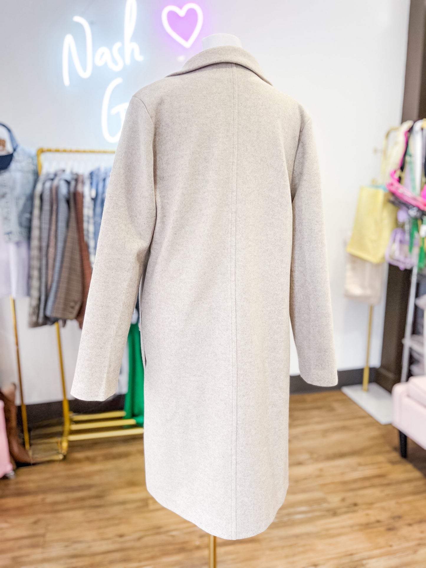 Beige coat on a mannequin in a store setting with 'Nash' and '6' neon signs.