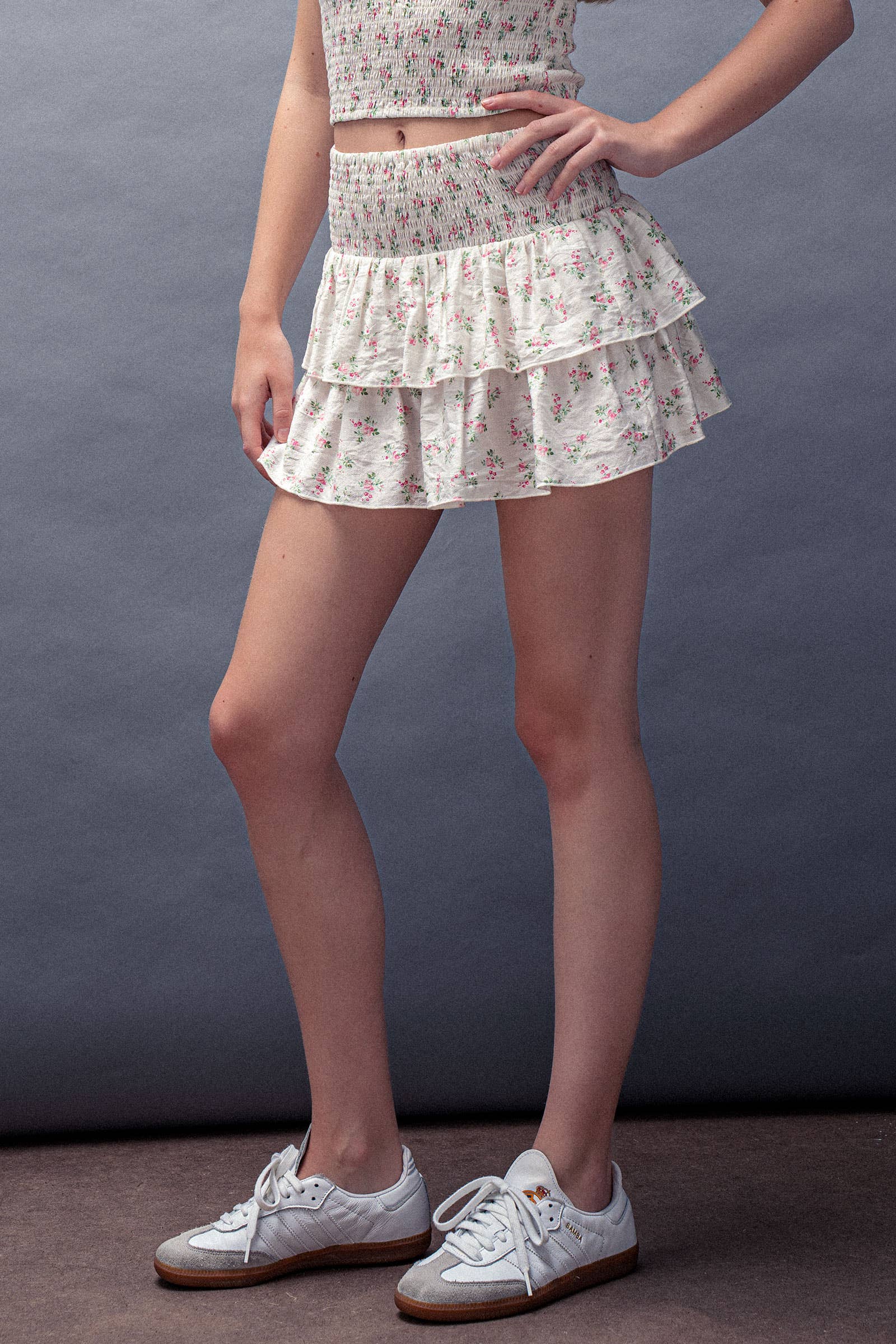 Person wearing a floral skirt and white sneakers against a gray background