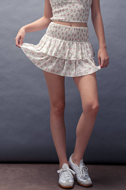 Person wearing a floral two-piece outfit with a skirt and top on a gray background