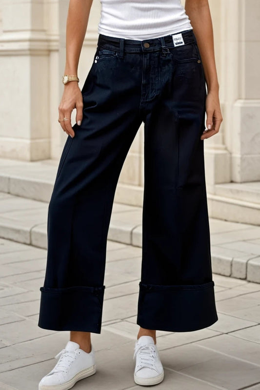 Woman wearing a white tank top and dark blue pants standing in front of a building.