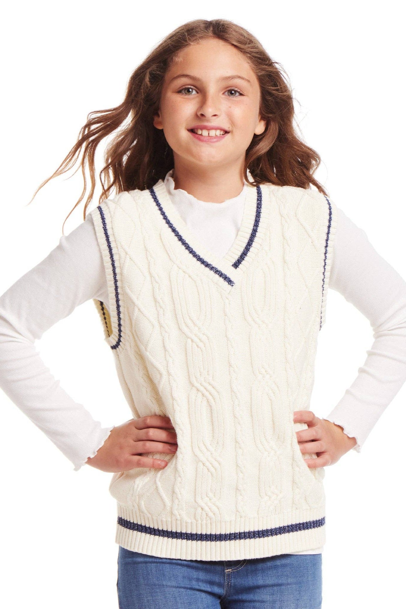 Young girl wearing a cream cable knit vest with navy trim on a white background