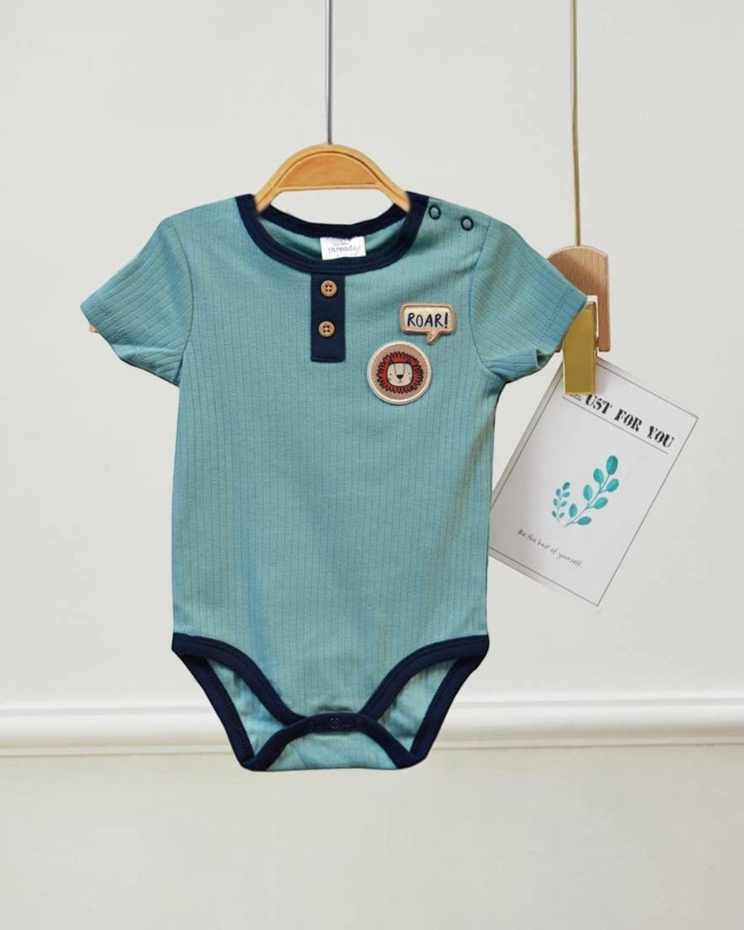 Blue baby onesie with lion design on a hanger against a white wall.