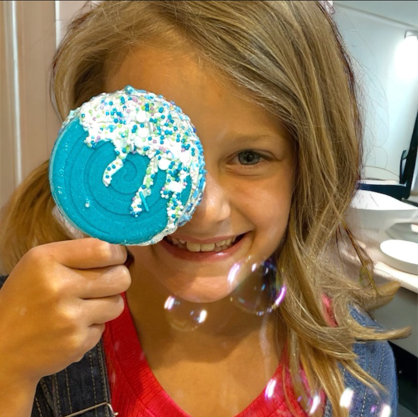 Child holding a blue cookie with sprinkles up to their eye, smiling.