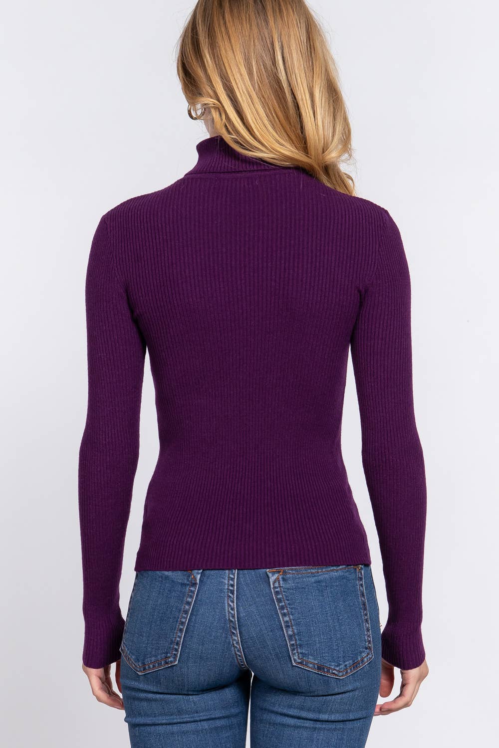 Person wearing a purple ribbed sweater and blue jeans on a white background