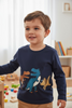 Child wearing a navy blue sweater with dinosaur designs in a room with toys and books.