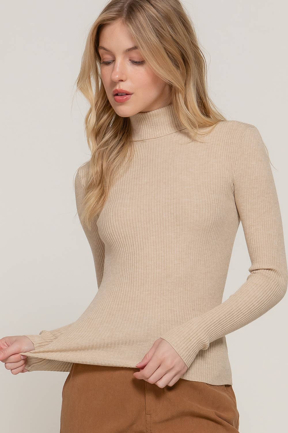 Woman wearing a beige ribbed turtleneck sweater against a plain background