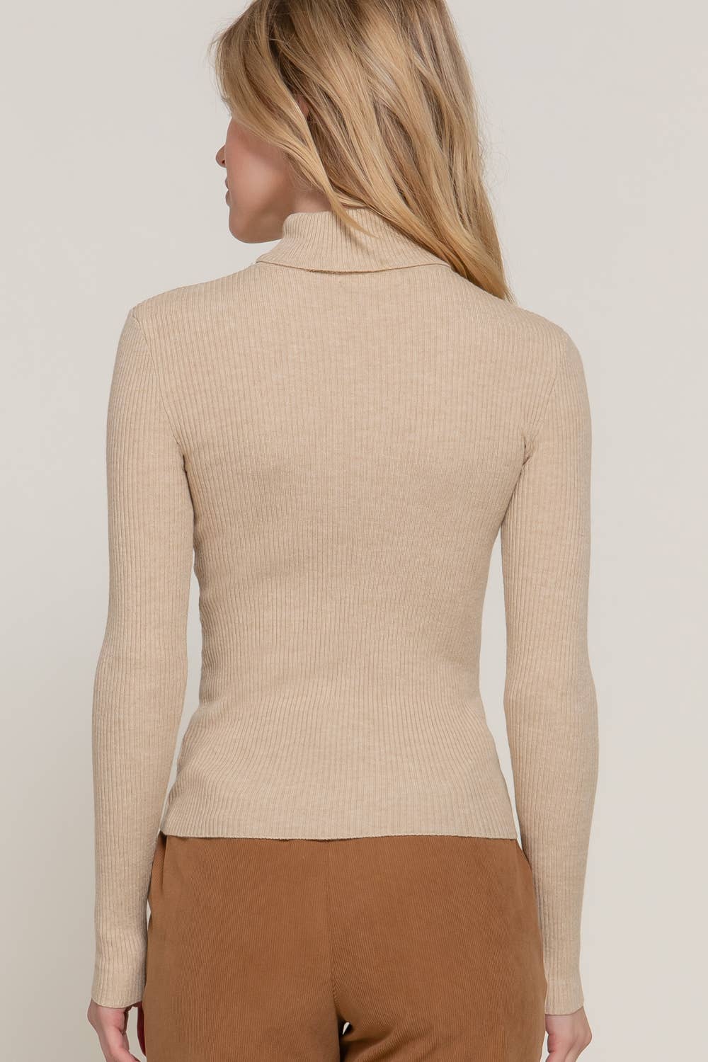 Woman wearing a beige ribbed turtleneck sweater against a plain background