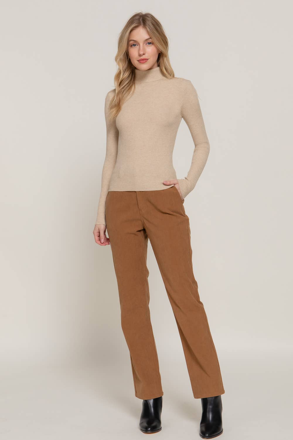Woman wearing a beige turtleneck and brown pants on a white background