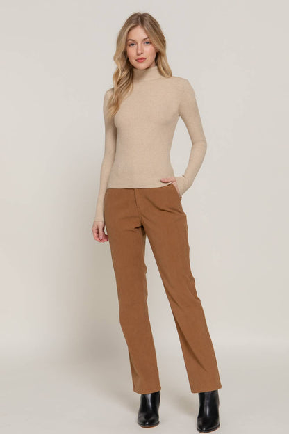 Woman wearing a beige turtleneck and brown pants on a white background
