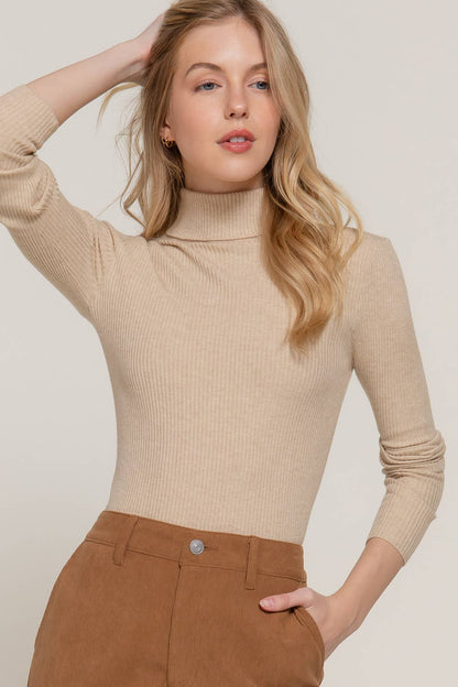 Woman wearing a beige ribbed sweater and brown pants against a plain background