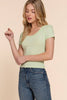 Woman wearing a light green top and blue jeans against a beige background