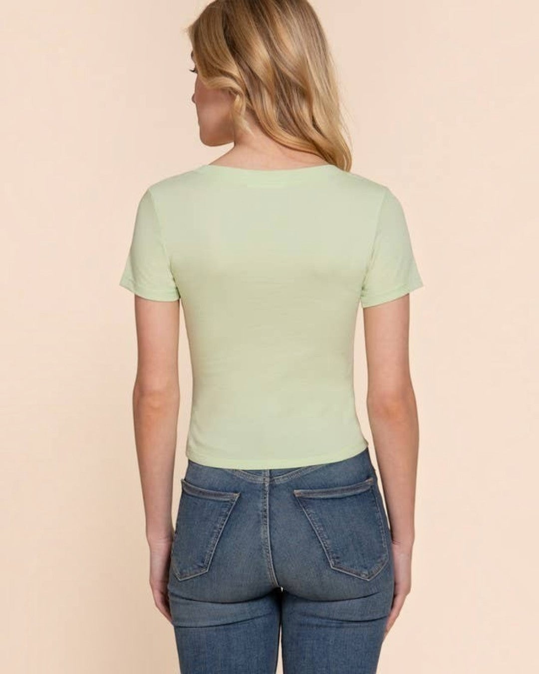 Woman wearing a light green t-shirt and blue jeans on a beige background