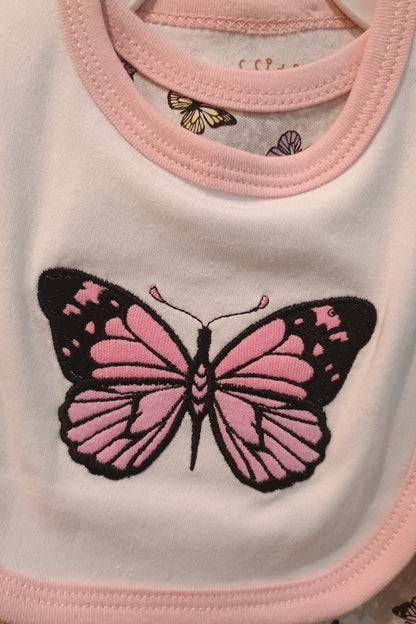 Close-up of a pink butterfly design on a white bib with pink trim.