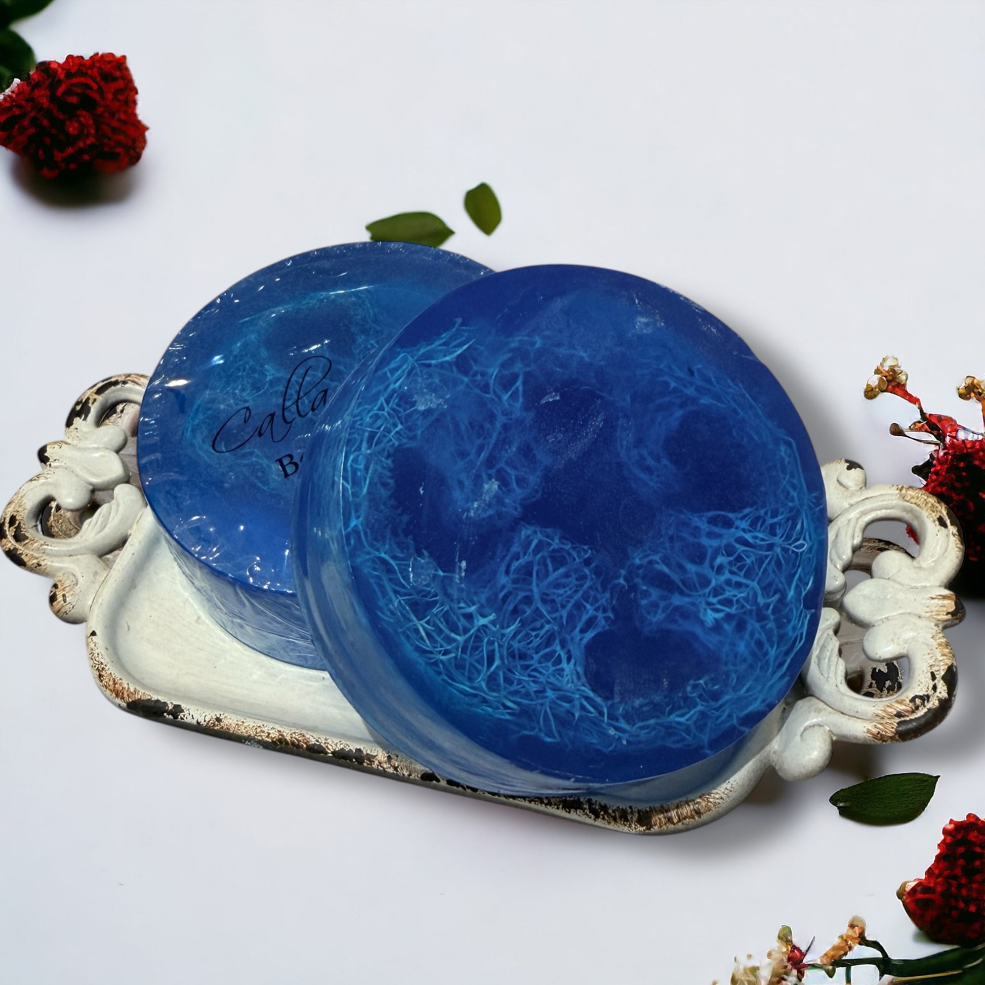 Two blue textured soaps on a decorative white tray with floral elements.