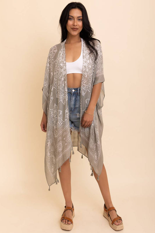 Woman wearing a light gray kimono-style garment over a white top and denim shorts on a beige background