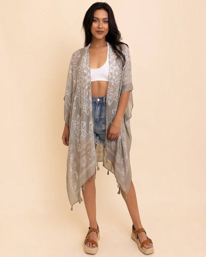 Woman wearing a light gray kimono-style garment over a white top and denim shorts on a beige background