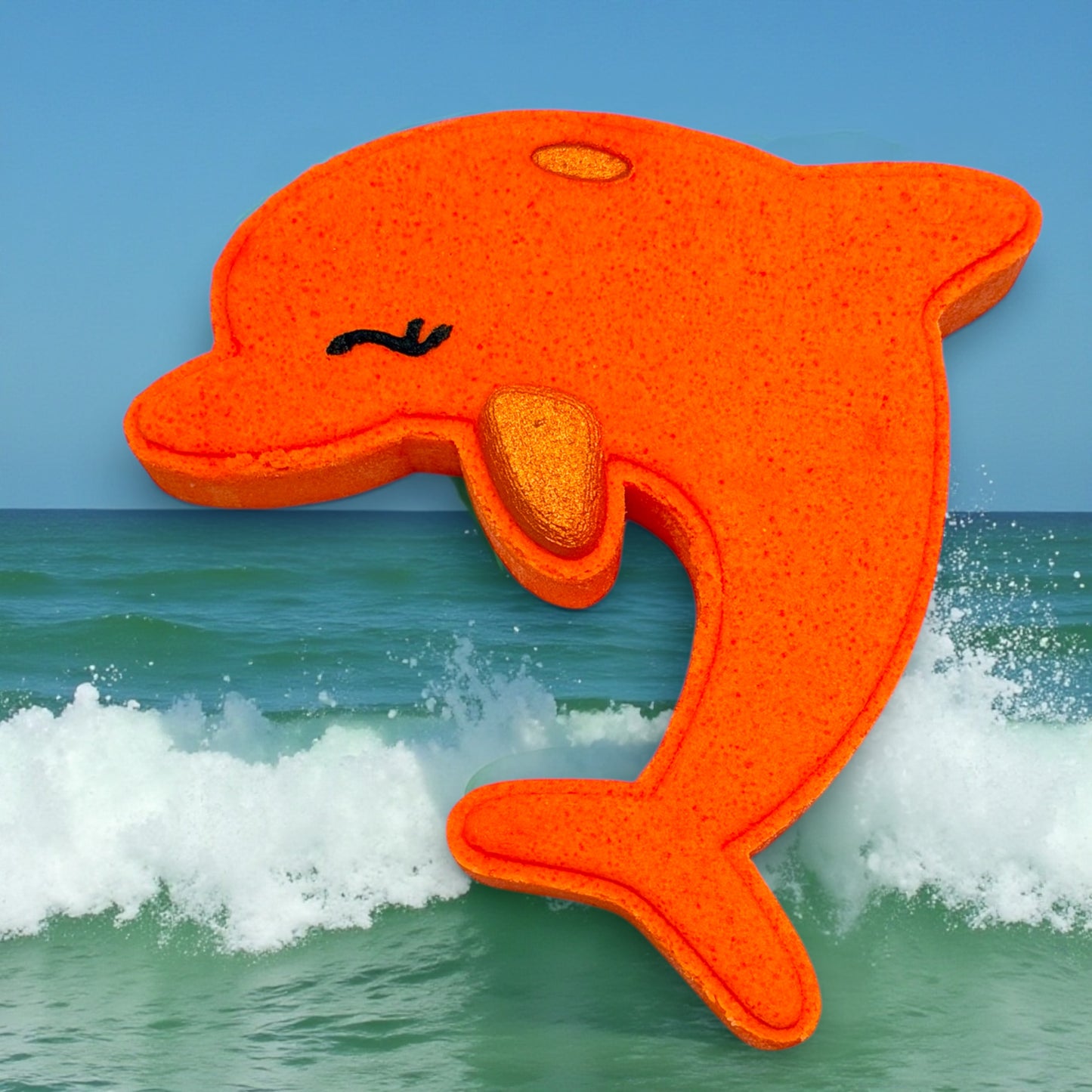 Orange dolphin-shaped bath bomb with a textured surface on a background of ocean waves and blue sky.