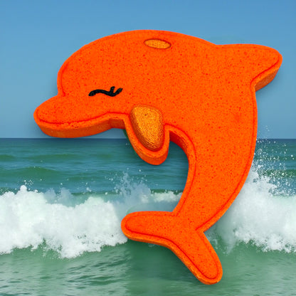 Orange dolphin-shaped bath bomb with a textured surface on a background of ocean waves and blue sky.
