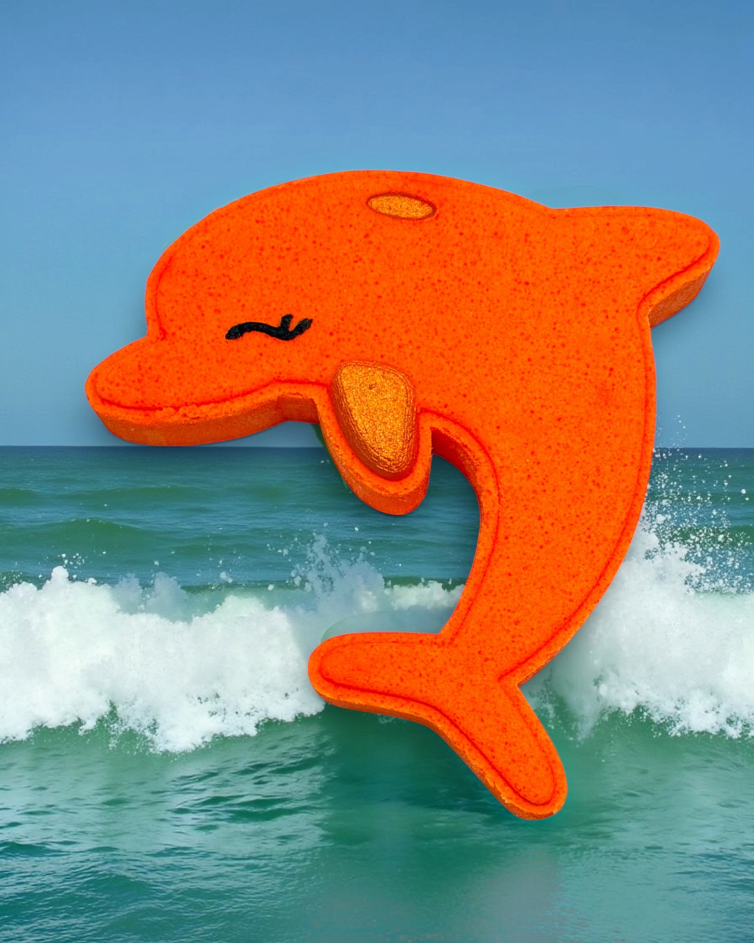 Orange dolphin-shaped bath bomb with a textured surface on a background of ocean waves and blue sky.
