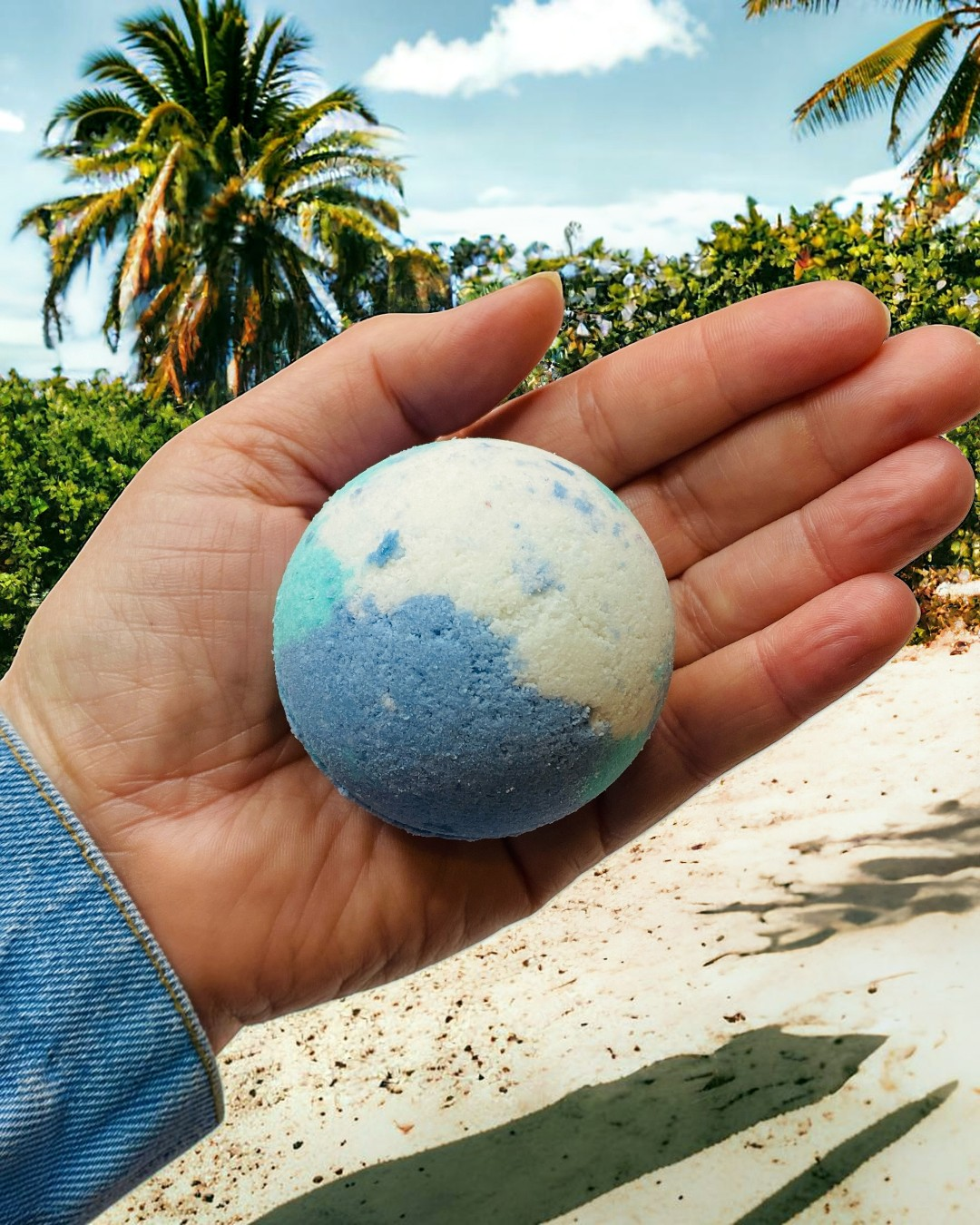 Calla Lily Cosmetics + CL kids Ocean Water bath bomb with blue and white swirls held in a hand at the beach