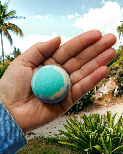 Calla Lily Cosmetics + CL kids Ocean Water bath bomb with blue and white swirls held in a palm against a tropical backdrop